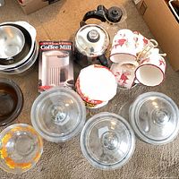 Group shot of all items on carpet including jars, bowls, mugs, French press, boxed coffee mill