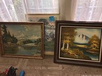 Three framed landscape prints leaning against window; left and right prints match lot description