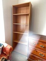 Full view of tall light oak bookcase beside dresser and chair