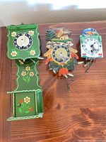 Front view of the three small hand-painted wooden clocks on tabletop