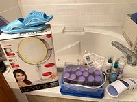 Overall lot showing boxed Revlon mirror, blue sandals, hot roller set, additional items