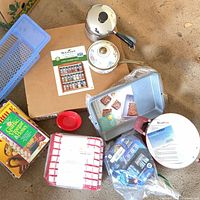 Group shot showing saucepans, baking pan, spice rack box, plastic basket, bowls, towel pack, cookbook packaging