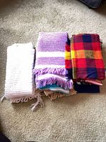 Four folded throws in white, lavender, plaid and blue tones