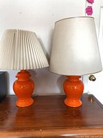 Both orange ceramic table lamps with shades displayed on surface