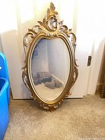Large ornate gold oval mirror with gilded resin frame, shown leaning against door