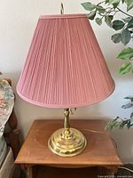 Full view of brass lamp with pink pleated shade on table
