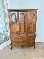 Front view of medium-brown oak French Provincial armoire with two parquet-paneled doors and two lower drawers