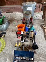 Overview of lot showing trash can on jack stands, funnels, bucket, grease gun, socket cases and accessories