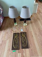 Two table lamps with beige shades and two peacock wall plaques on floor