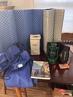 All items arranged on table: folding foam mat, lantern, solar panel, battery pack, canvas cover, book