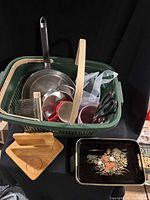 Overall lot showing basket with cookware, utensils, mugs, wooden spacer, tray partly visible