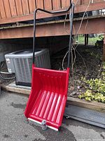 Front view of red snow scoop standing upright showing handle, scoop, and wear strip