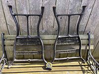 Pair of cast iron legs leaning on wooden bench showing overall form and size tape for scale