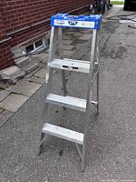 Full view of three-step aluminum ladder standing on pavement