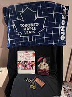 Overall lot showing Toronto Maple Leafs pillowcase draped, two books, and dart set