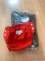 AppleCheeks red diaper cover atop sealed AlvaBaby gray diaper package