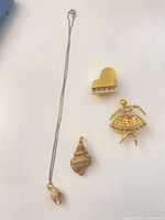 Full view showing all four jewellery pieces: silver chain with shell pendant, gold-tone heart pendant, gold-tone ballerina brooch