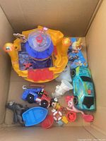 Box containing assorted plastic toys including playset base, vehicles, figures