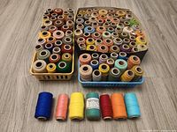 Three baskets filled with assorted colorful thread spools displayed on floor, additional eight spools lined in front
