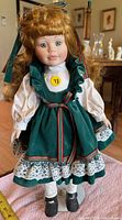 Full frontal view of dressed porcelain doll on stand