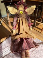 Front view of handmade cloth angel doll seated, showing dress, apron, wings, and button detail