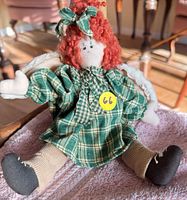 Full view of rag doll seated on towel showing dress, wings, shoes