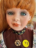 Close-up of doll face showing hair, eyes, painted features, brooch and collar