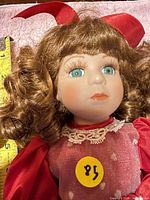 Close-up of doll head showing brown curls, blue eyes and red hair bow with measurement tape for scale