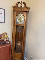 Full view of oak-tone grandfather clock with swan-neck pediment