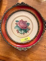 Front view of round framed needlepoint showing rose design and metal-trimmed frame