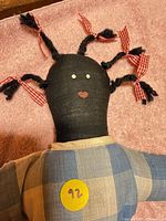 Close view of doll head showing black cloth, yarn braids, gingham ribbons, stitched face