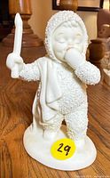 Full view of figurine standing on base, child in textured suit holding candle