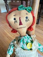 Close-up of doll head showing facial features, red yarn hair, green bow