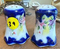 Front view of both porcelain shakers showing floral pattern, blue glaze, yellow lot sticker