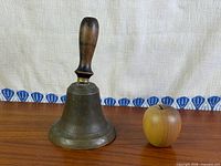Full view of brass handbell beside wooden apple for scale