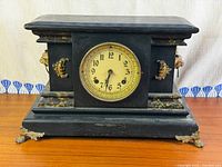 Front view of black mantel clock showing dial, case and feet
