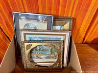 Box with multiple framed artworks and empty ornate frame