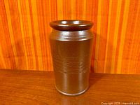 Full view of cylindrical brown stoneware vase on wood surface