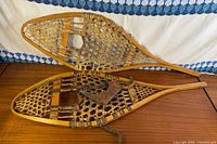 Overview of both snowshoes showing wood frames, rawhide webbing, leather bindings