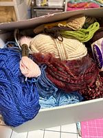 Open box showing multiple yarn skeins in blue, cream, green, tan, red tones