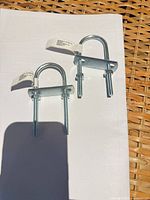 Two galvanized U-bolts with plates and nuts on white background showing full items and attached tags