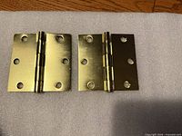 Front view of both brass-plated hinges showing mounting holes and finish