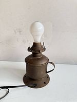 Front view of bronze metal table lamp showing cylindrical body, handle, base, socket, cord