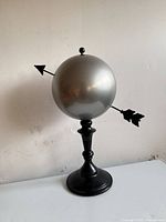 Full view of silver globe with black arrow and stand