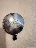 Top view of chrome bicycle bell showing embossed graphic and black striker