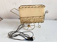 Front view of brass-tone wire frame cart lamp with beige shade and cord