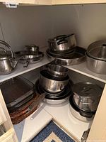 Corner cupboard shelf showing stacked stainless steel pots, pans, mixing bowls and lids
