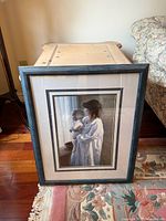 Full view of framed print leaning against chest, showing frame, mat, and image