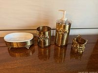 Four Stylebuilt gold-tone bathroom accessories grouped on table