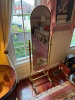 Full view of brass floor standing oval mirror near window